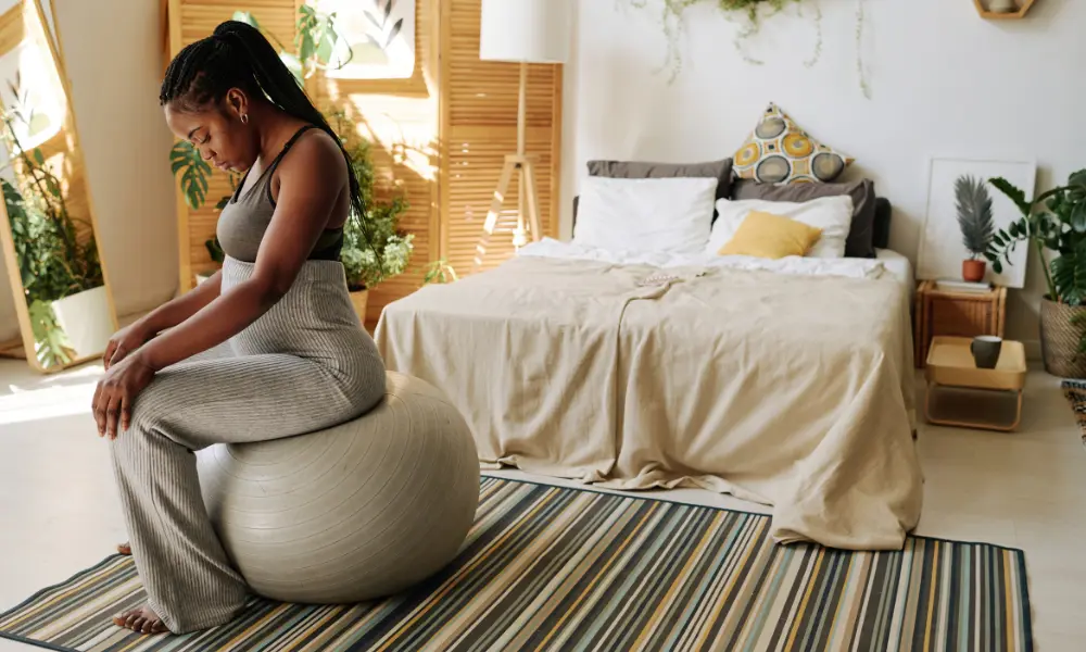 A woman sits on an exercise ball in her room