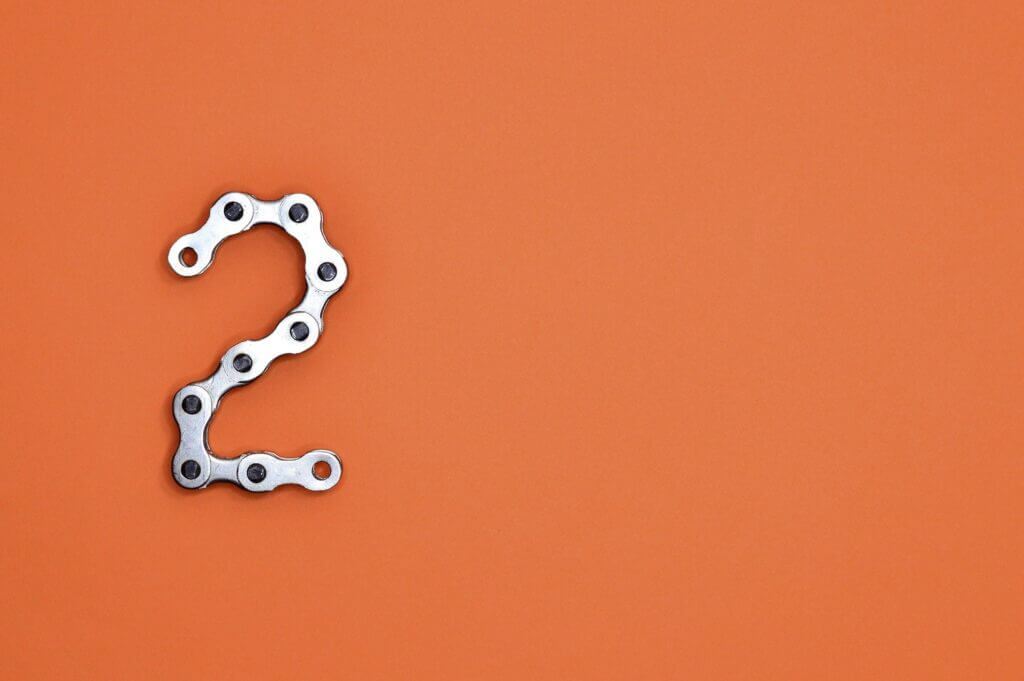Bright orange background silver bike chain forms number two on left side of image
