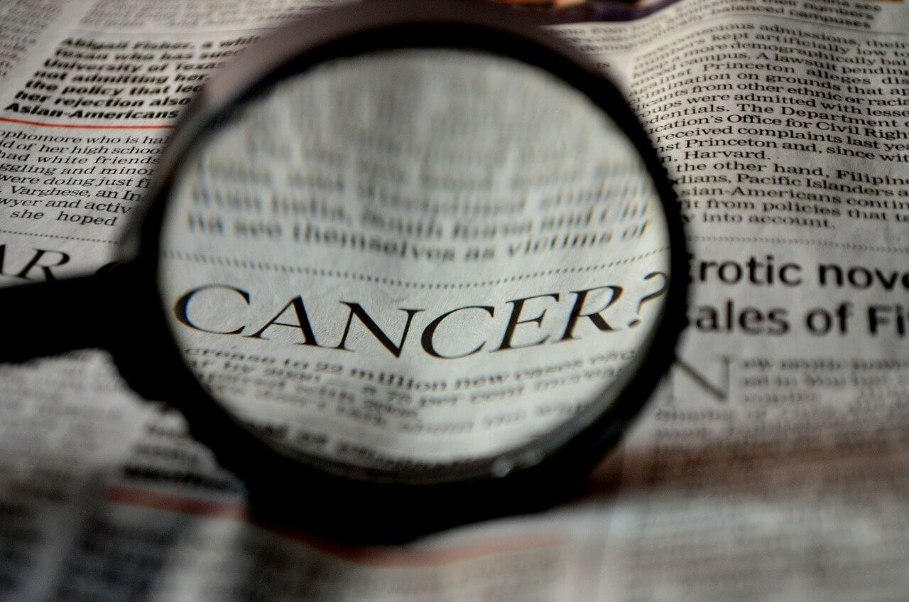 Magnifying glass in foreground held over newspaper the word Cancer is enlarged in magnifying glass