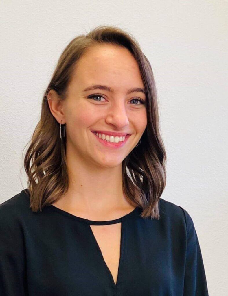 Headshot photograph of Dr Ellen Meisner with shoulder length brown hair curled smiles in black top