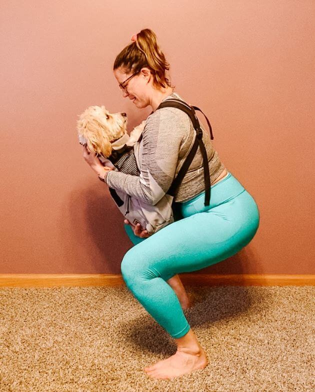 Women in squatting position looking at her dog who is in a carrying case on her chest