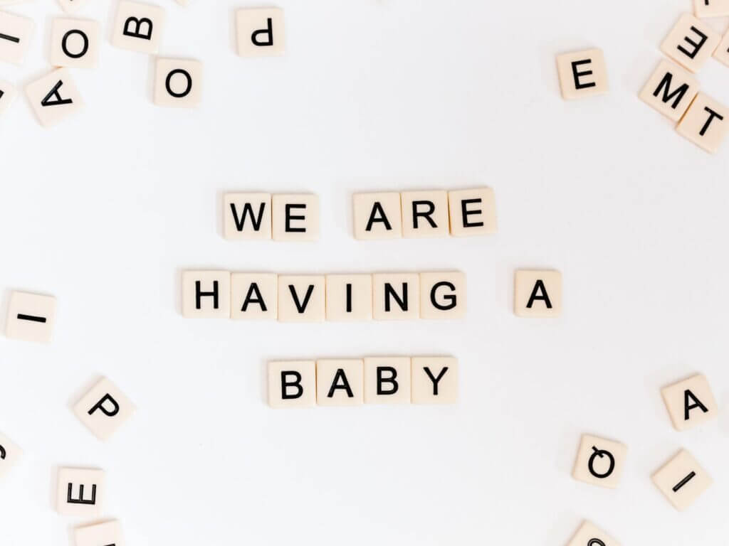 White background with tan scrabble tiles with black block letters spell out “we are having a baby”