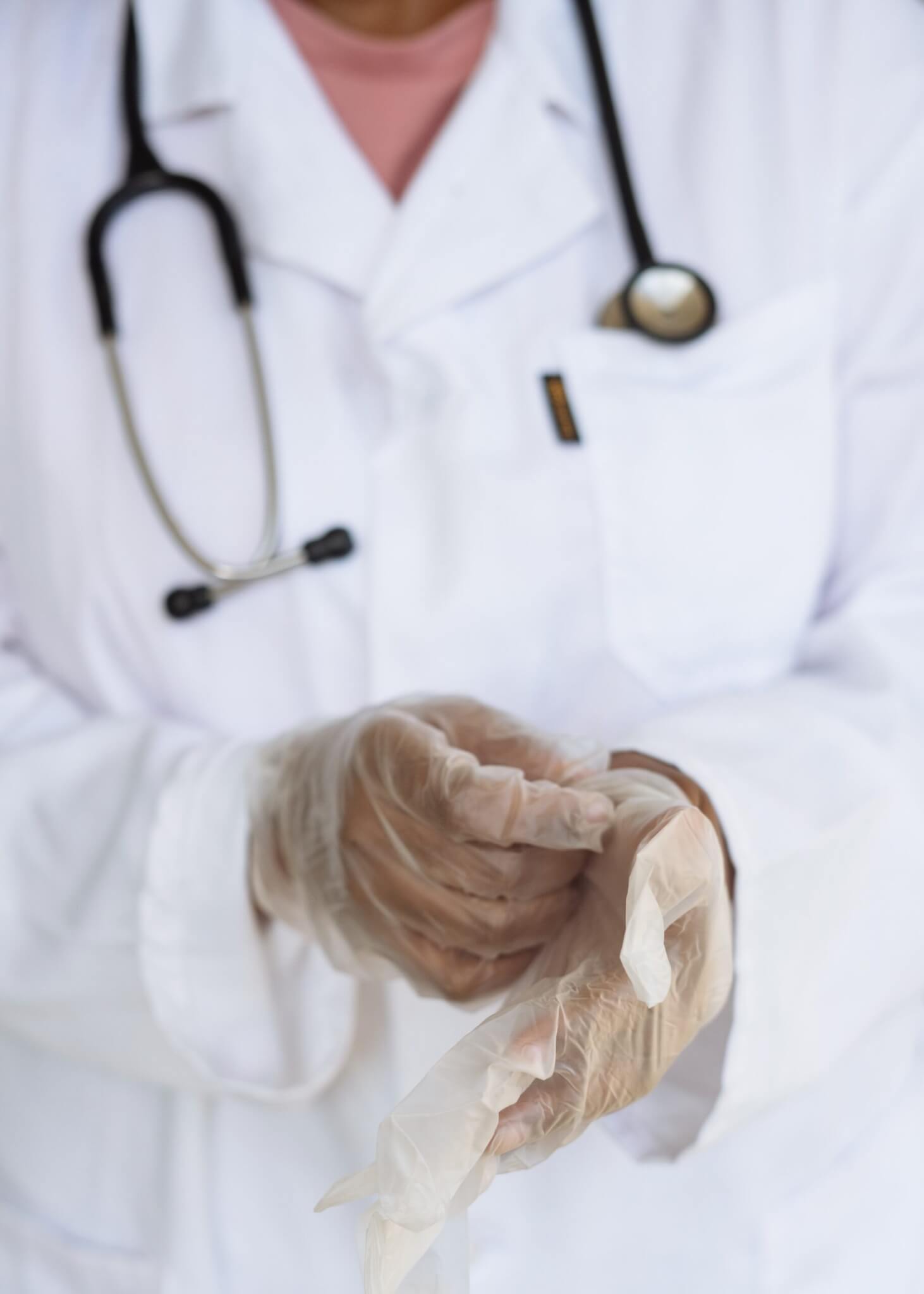 close up of doctor in white coat with stethoscope around neck picture focused on the gloved hands
