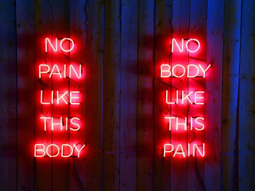 Red neon sign on wooden wall in dark room reads: no pain like this body no body like this pain