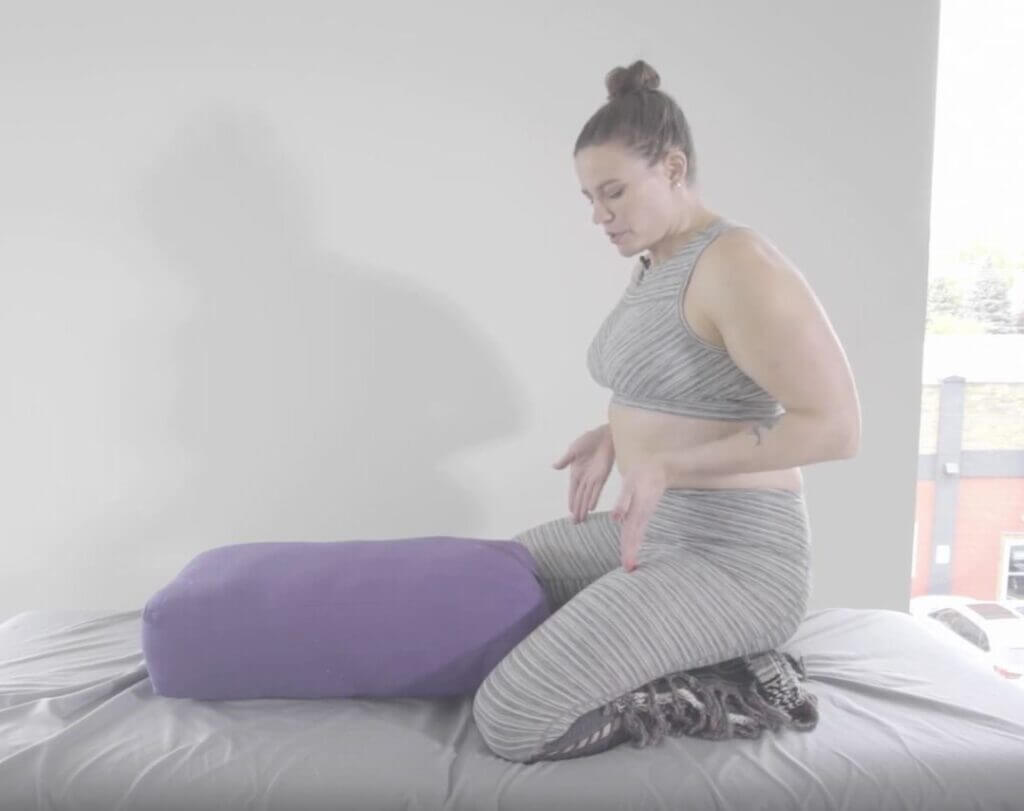 Purple yoga block sits between her knees about 6 inches toward pelvis knees bent buttocks on toes