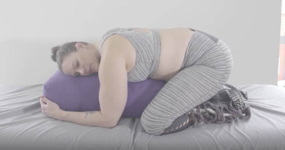 Laura on knees blanket between buttocks and feet chest rests forward on large purple yoga bolster