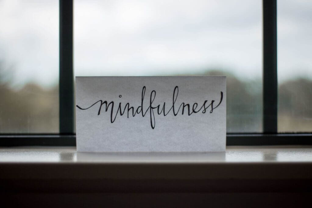 White piece of paper sitting in front of a window black calligraphy in large font reads mindfulness