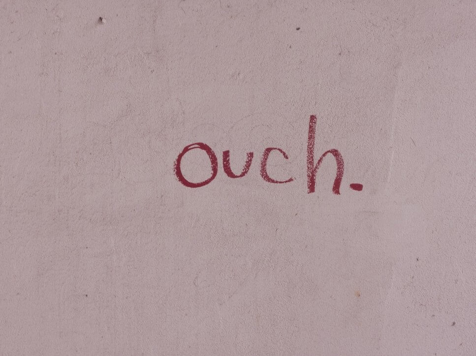 Pale pink painted wall background with the word ouch written in red on the wall