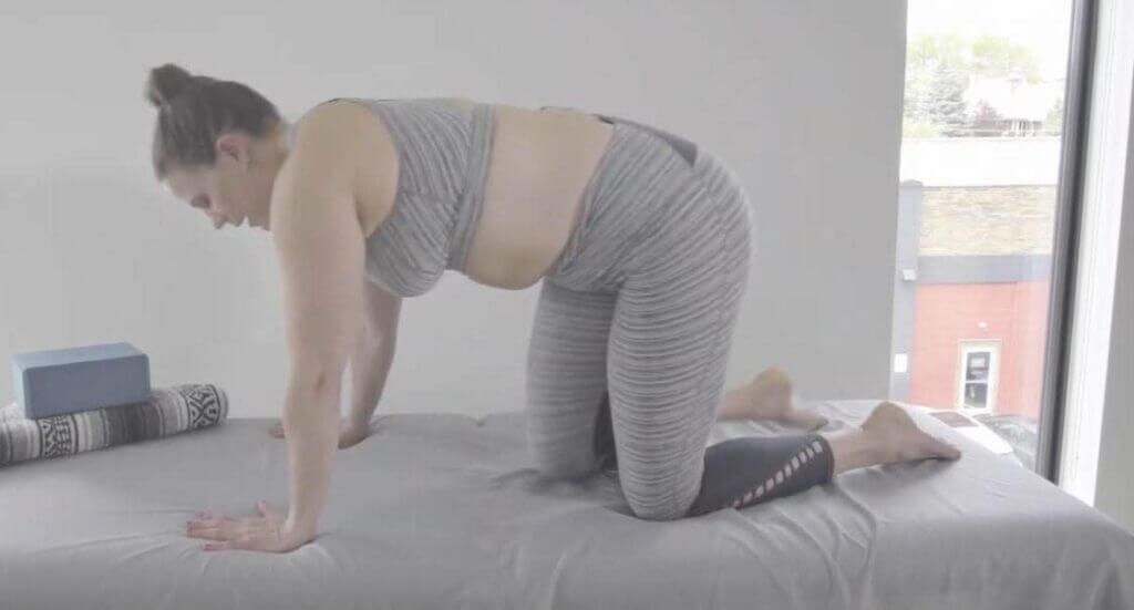 Laura on hands and knees shoulder width apart on mat in gray yoga outfit with blocks in corner