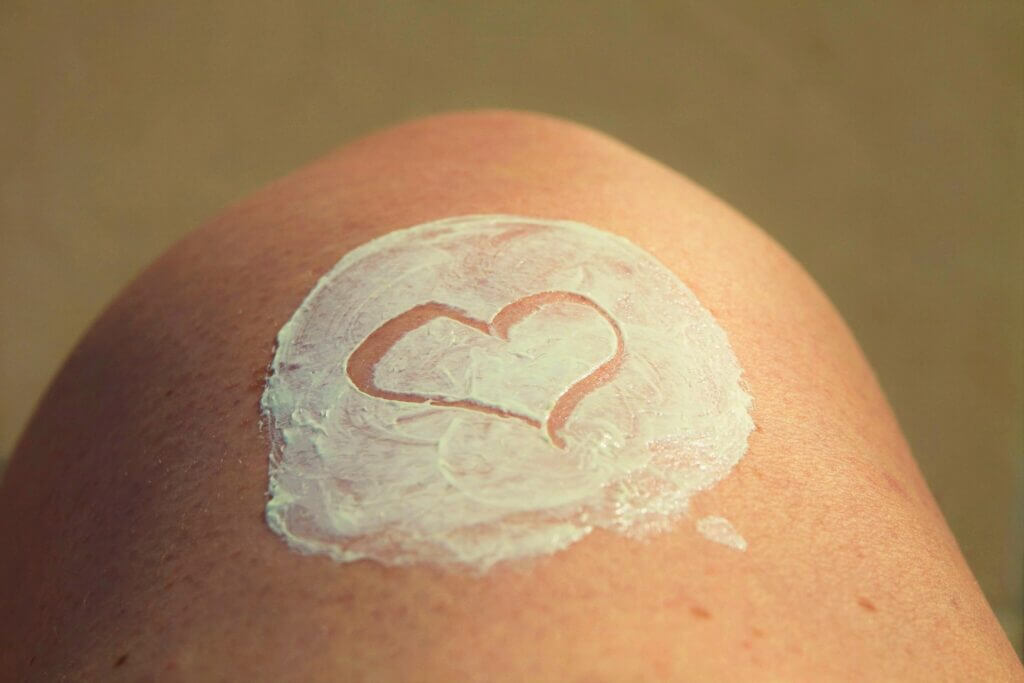 Close up of exposed knee with a thick circle of lotion on top and a heart is drawn in the lotion