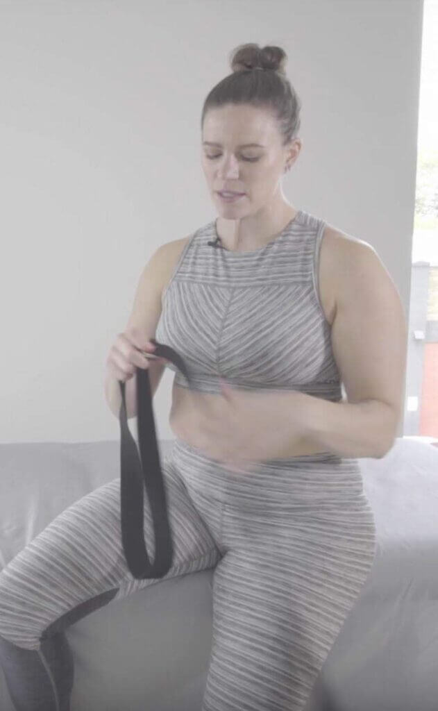 Laura holding black yoga strap in hands strap is in a loop shape tail hanging loose near left hand