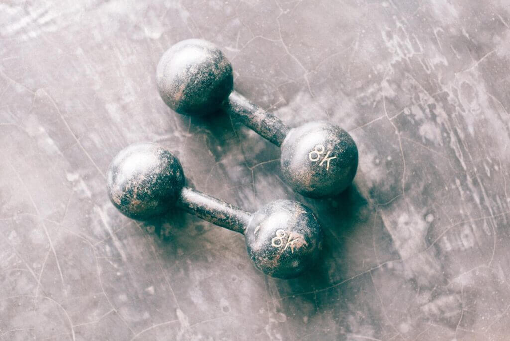 two rounded metal grey dumbbells lay on the floor