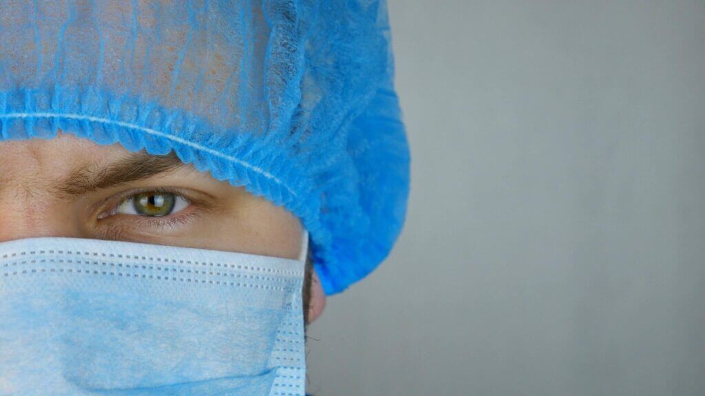 Close up image of one eye, part of a hair covering, and part of a face mask of medical professional