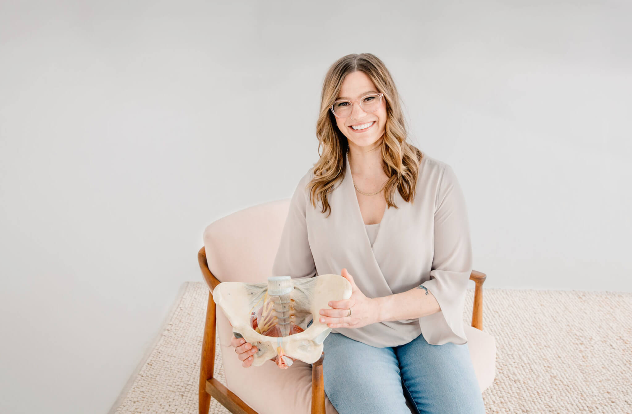 Dr. Laura sitting on light pink wood chair with skeletal model of pelvis in hands