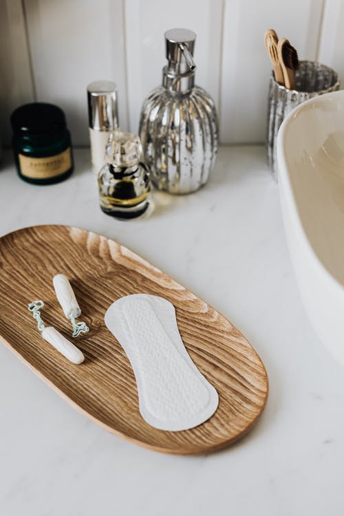sustainable menstrual products sit on wooden platter on bathroom counter