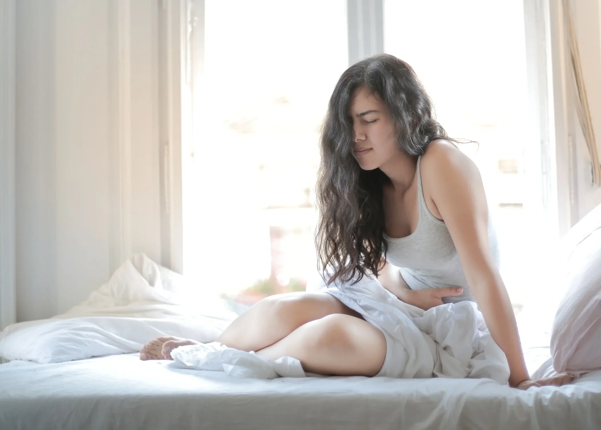 A woman lays on a bed in pain from PMOS symptoms