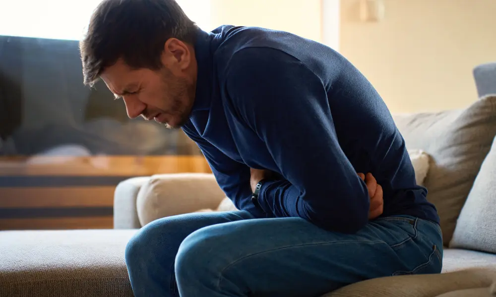 Man holding his stomach area and leaning over in pain while sitting down