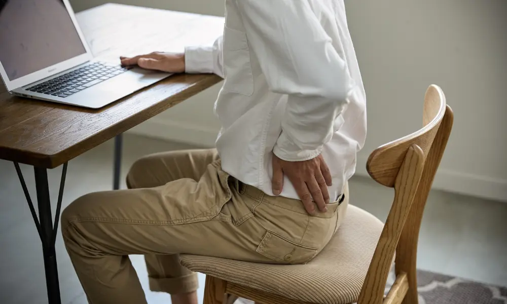 Someone sits at a desk while holding their lower back in pain