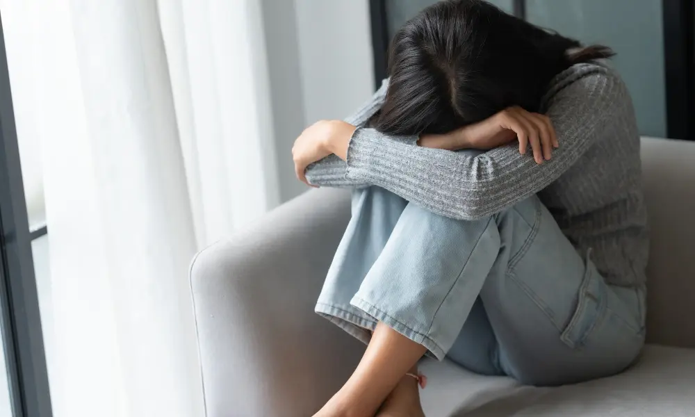Person sitting curled up on a couch and hiding their face