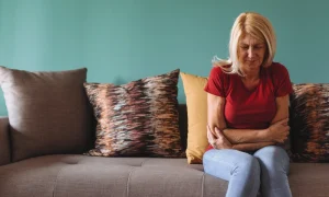 Woman sitting on a couch alone holding herself with a look of pain or frustration
