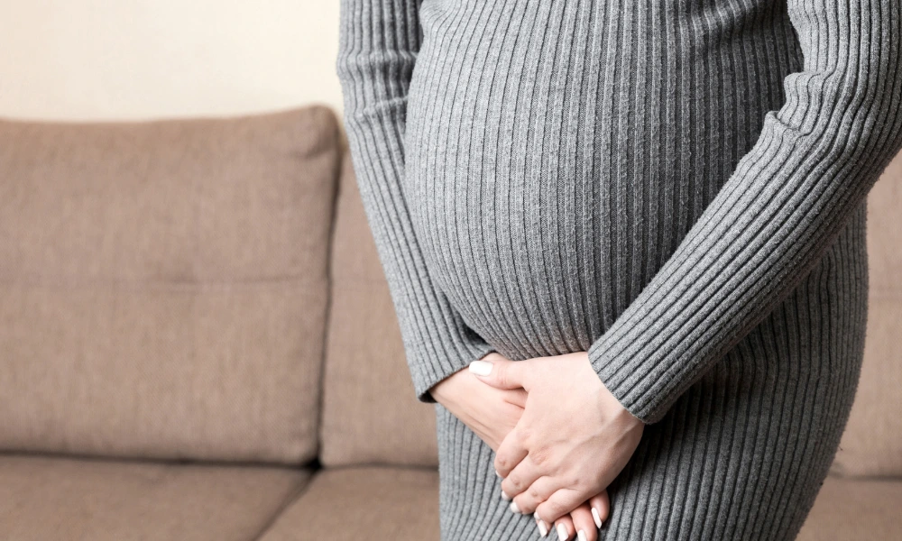 Pregnant individual holding their lower pelvic area with urgency