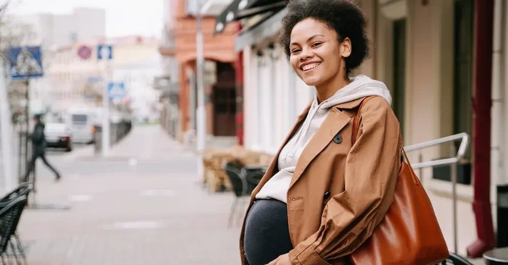 Pregnant individual smiling while standing on a sidewalk