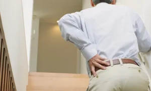 Man in the middle of climbing stairs holding his lower back in pain