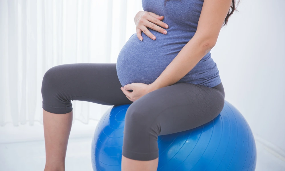 A pregnant individual sits on an exercise ball