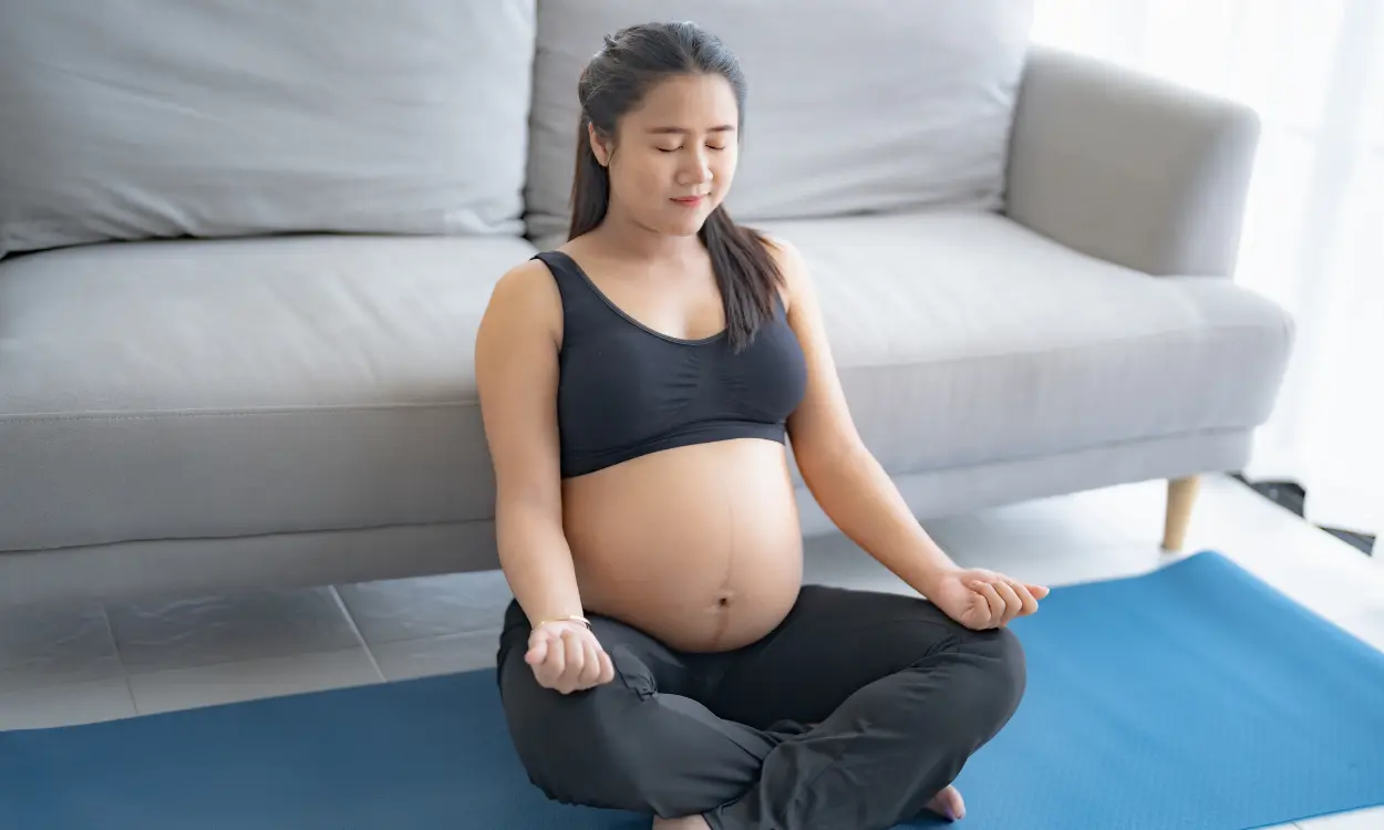 Pregnant person sits on a yoga mat and meditates