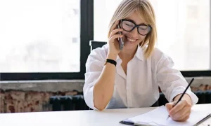 A woman talks on the phone while writing notes