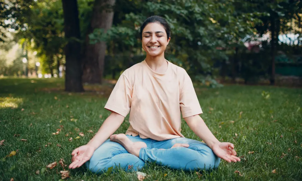 yoga-relax-happy A person sits outside doing meditation while smiling